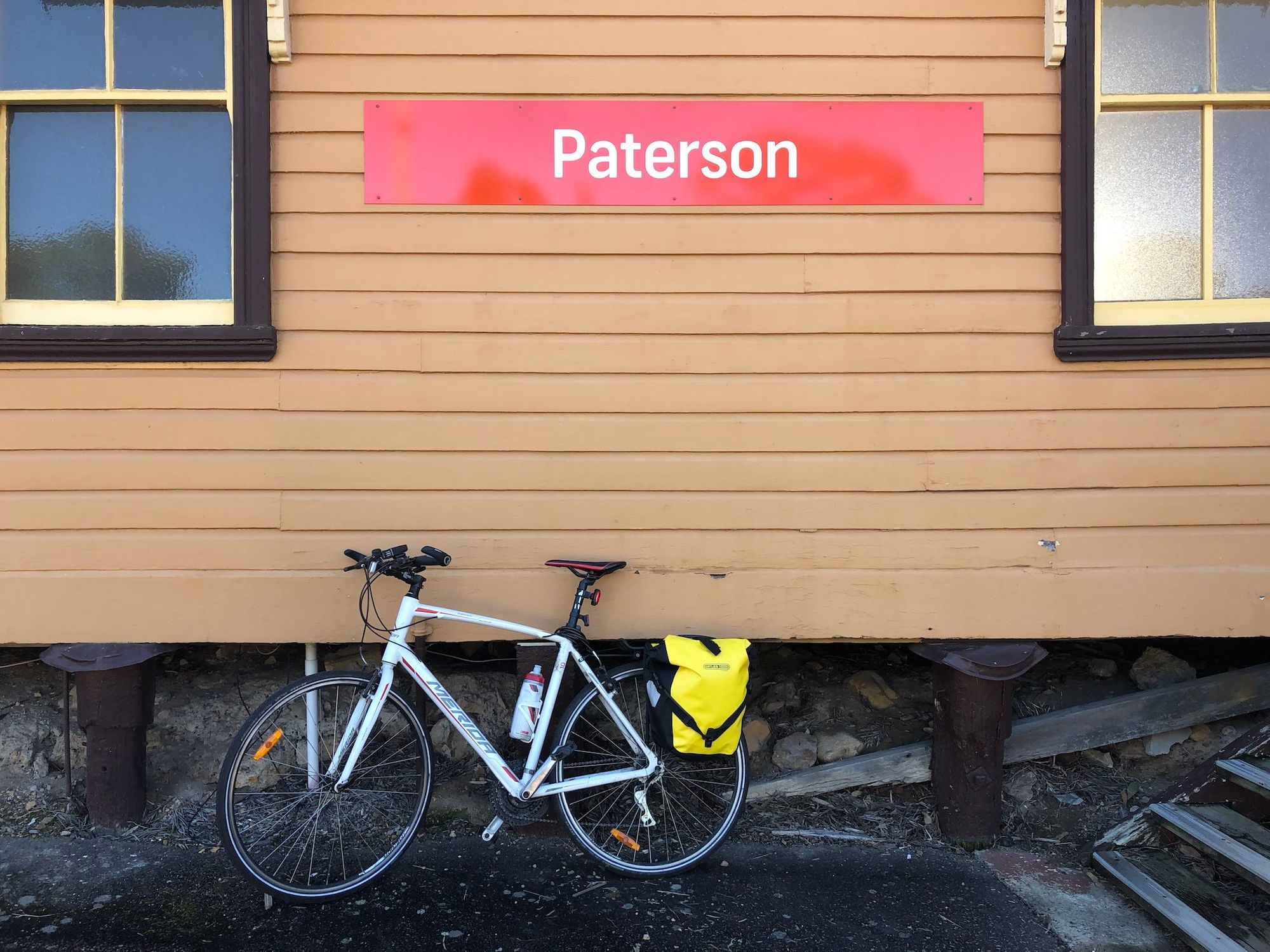 Bicycle with panniers, in front of wooden train station building, labelled "Paterson"